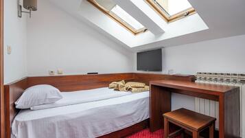 Una habitación pequeña con cama, escritorio, televisor y tragaluz.