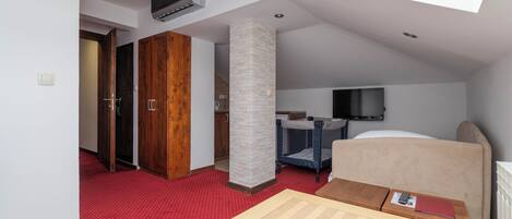 Quarto de hotel com claraboia, uma cama, escrivaninha, cadeira, televisão e guarda-roupa.