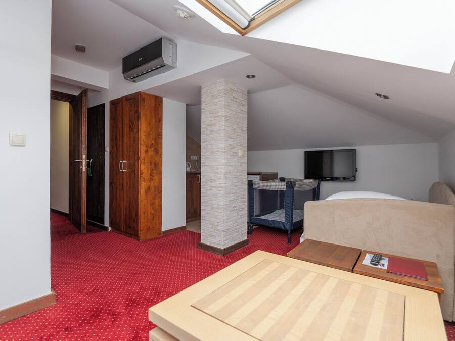 Quarto de hotel com claraboia, uma cama, escrivaninha, cadeira, televisão e guarda-roupa.