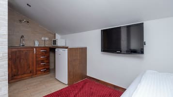 Een kleine hotelkamer met kitchenette, flatscreen-tv, bed en een rood tapijt met patroon.