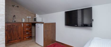 Quarto de hotel compacto com cozinha compacta, televisão de tela plana, uma cama e um tapete vermelho estampado.