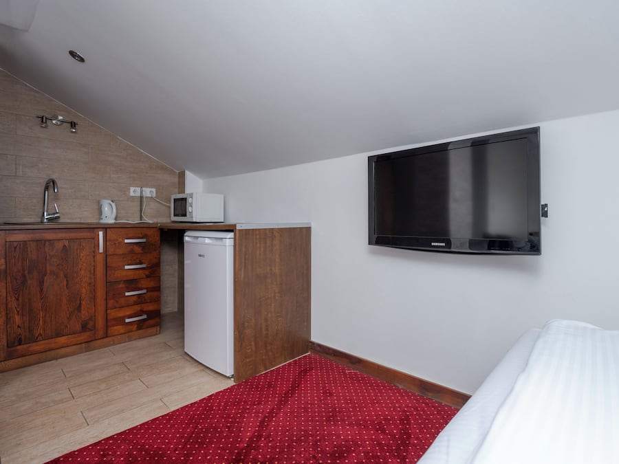 Een kleine hotelkamer met kitchenette, flatscreen-tv, bed en een rood tapijt met patroon.