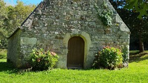 Eine steinerne Kapelle mit Glockenturm, rundbogigem Eingang und einer grünen Umgebung.