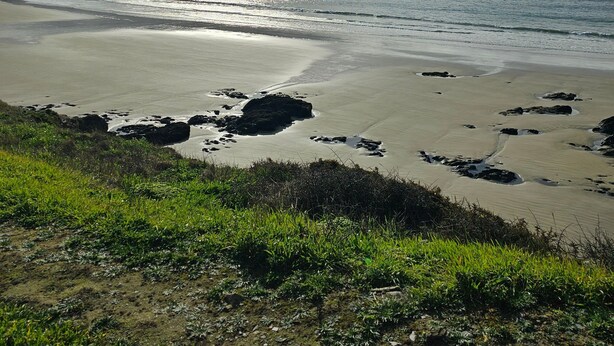 Ein Strand mit blauem Himmel, ruhiger See und Felsen.