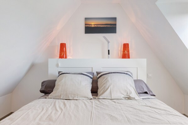 Une chambre avec un plafond en pente, un lit avec deux oreillers, une table de chevet et un tableau accroché au mur.