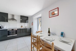 Une cuisine moderne avec un coin repas, des appareils en acier inoxydable et une table blanche dressée pour quatre personnes.