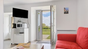 Ein Zimmer mit einem roten Sofa, einer weißen Kommode mit Fernseher und einer Tür zu einem Garten.