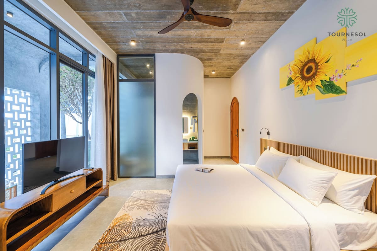 A modern hotel room with a large bed, a TV, and a ceiling fan.
