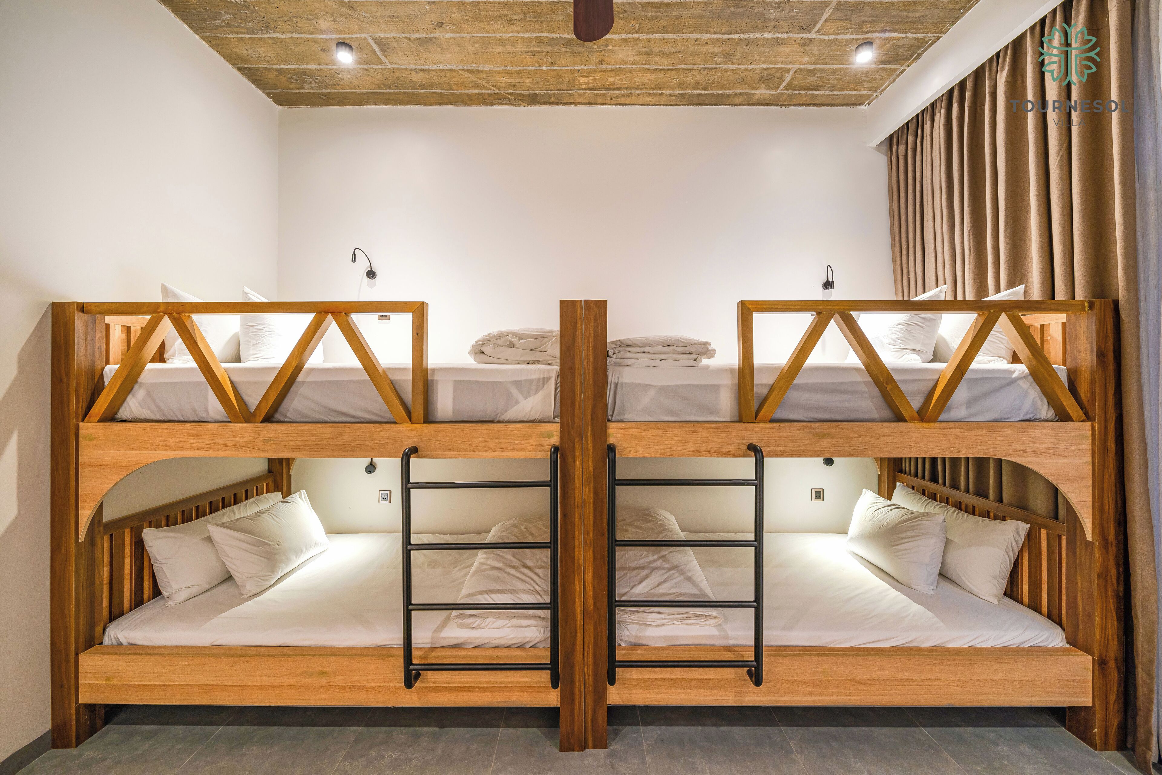A bunk bed room with wooden frames and white bedding. There are two beds, one on top of the other, and a ladder between them.