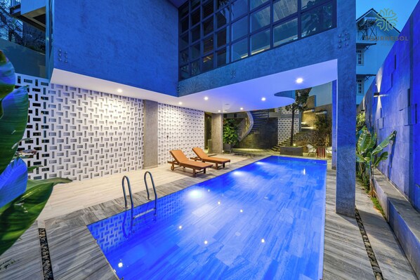 Une piscine intérieure moderne, dotée de murs au design géométrique, de chaises longues et d’un escalier menant à un niveau supérieur.