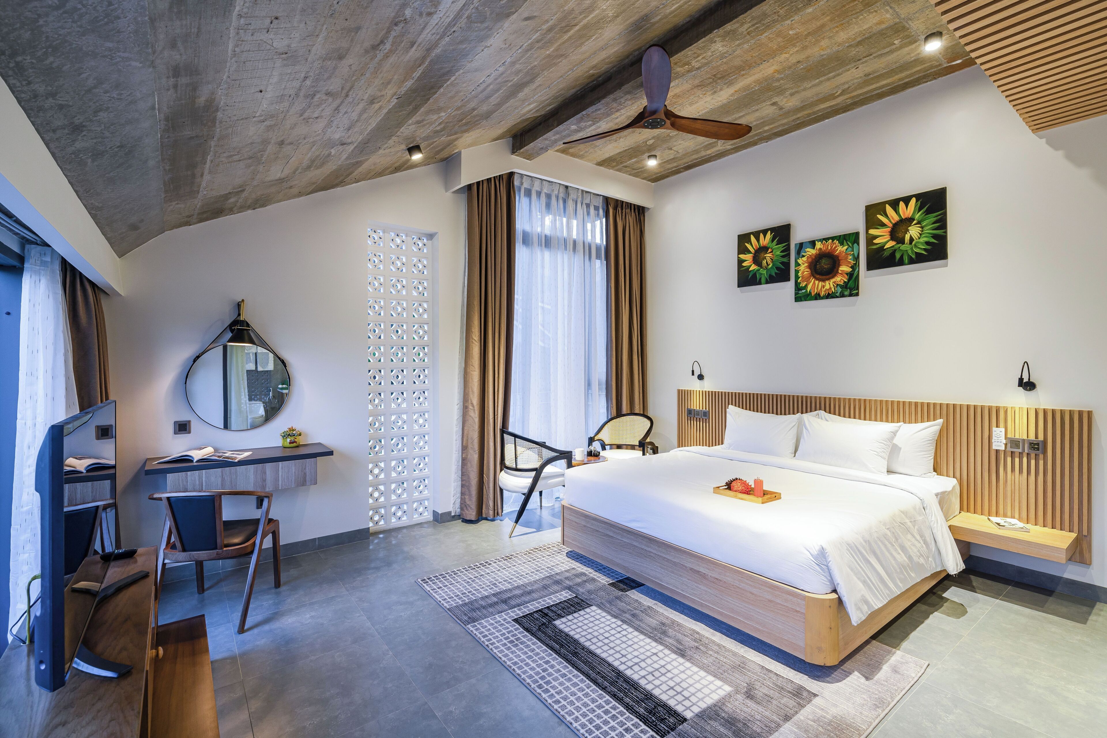 A modern hotel room with a large bed, a desk with a computer, a chair, and a ceiling fan.