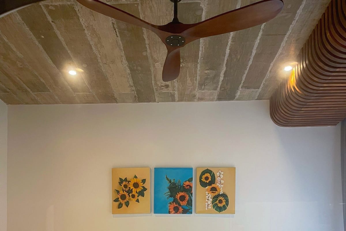 A hotel room with two beds, a ceiling fan, and three wall-mounted paintings.
