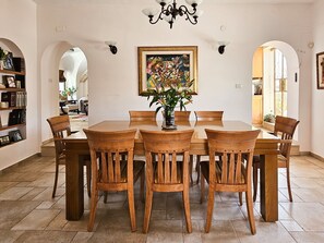 A dining room with a wooden table and chairs, a chandelier, and a framed painting above the table. - Family Friendly with Terrace in Old City by FeelHome (Jerusalem)