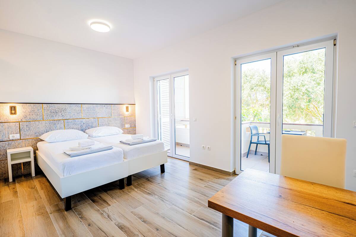 Een moderne slaapkamer met een groot bed, een houten tafel en een balkon met uitzicht op bomen.