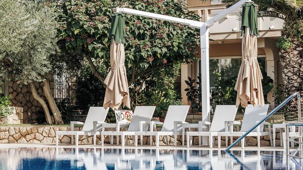 A poolside area with lounge chairs and umbrellas, a no swimming sign, and a stone wall. - Resort Trcol (Novalja)