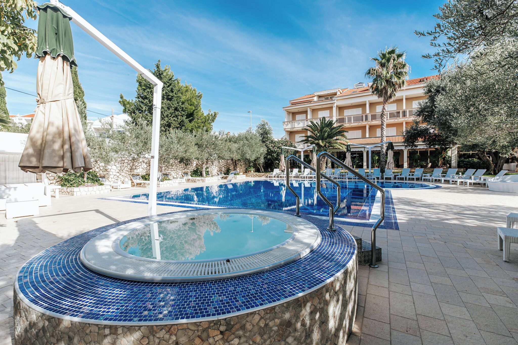 A swimming pool with a tiled edge, lounge chairs, and a building in the background.