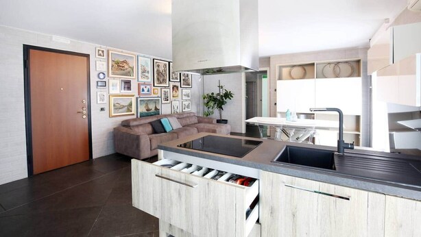 Una cocina moderna con una isla central, una zona de comedor con mesa blanca y una sala de estar con sofá y obras de arte en la pared.