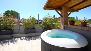 Una azotea con jacuzzi, plantas en macetas y una vista despejada del paisaje urbano.