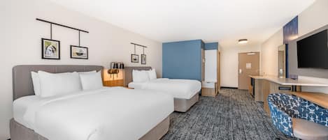 A hotel room with two beds, a desk, a chair, a TV, and artwork on the walls.