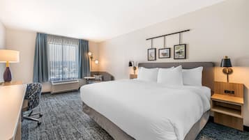 Een hotelkamer met een groot bed, een bureau, een stoel, een tafeltje en een raam met gordijnen.