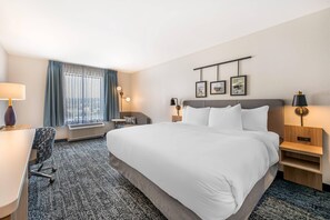 A hotel room with a large bed, a desk, a chair, a small table, and a window with curtains. - Sleep Inn & Suites Harrisburg Airport - Hershey South (Middletown)