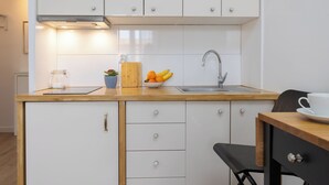 A compact kitchen with white cabinets, a wooden countertop, a sink, a cutting board, a bowl of fruit, and a coffee cup. - New World Apartament (Warsaw)