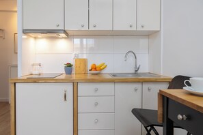 A compact kitchen with white cabinets, a wooden countertop, a sink, a cutting board, a bowl of fruit, and a coffee cup. - New World Apartament (Warsaw)