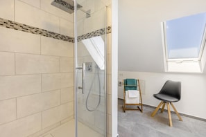 A modern bathroom with a glass shower enclosure, a small wooden chair, and a skylight. - Apartment 'Ferienwohung Seidel' with Balcony and Wi-Fi (Angermünde)