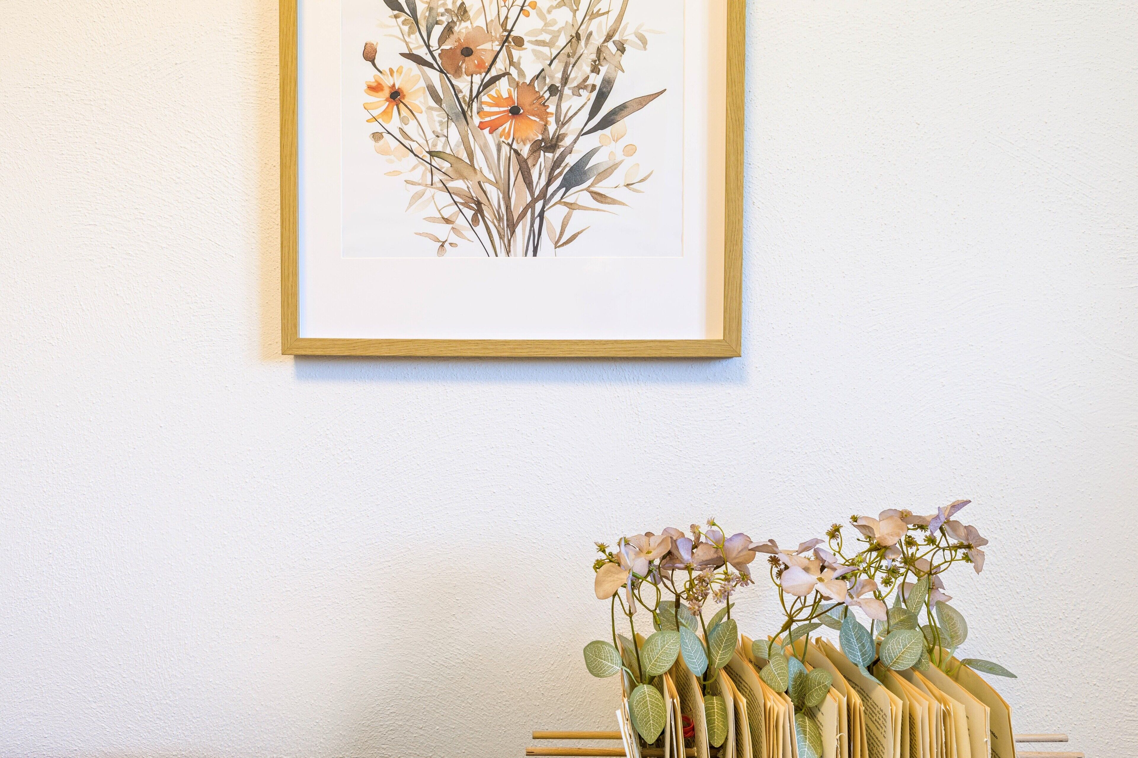 A framed botanical illustration and a stack of books with flowers on a white wall.