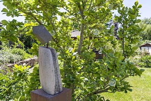 A garden with a stone sculpture, lush greenery, and a house in the background. - Apartment 'Ferienwohung Seidel' with Balcony and Wi-Fi (Angermünde)