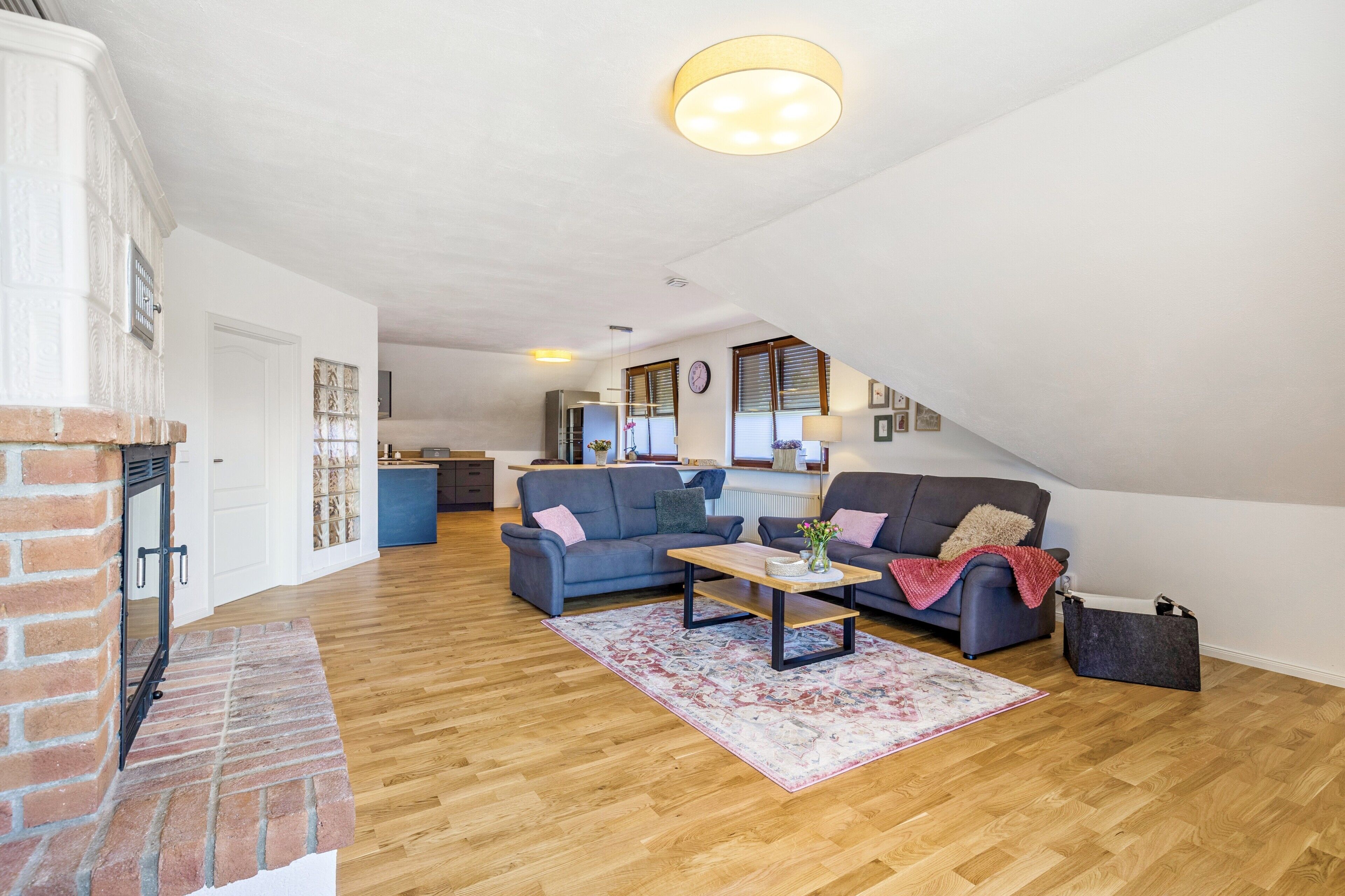 Een ruime loft met hoge plafonds, een open haard, een keuken op de achtergrond en een zithoek met banken en een salontafel.