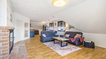 Een ruime loft met hoge plafonds, een open haard, een keuken op de achtergrond en een zithoek met banken en een salontafel.