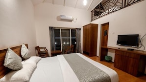 Een hotelkamer met een bed, een televisie, een bureau en een balkon met uitzicht op de nachthemel.