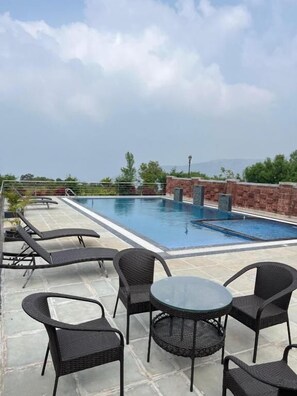 A rooftop pool area with lounge chairs and tables, surrounded by stone walls and greenery. - Kabila Agro Tourism (Mahabaleshwar)