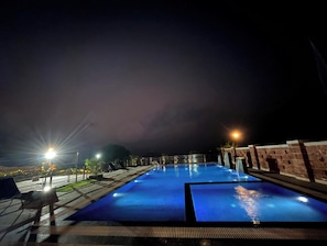 A nighttime swimming pool with clear water, surrounded by a brick wall and illuminated by street lamps. - Kabila Agro Tourism (Mahabaleshwar)
