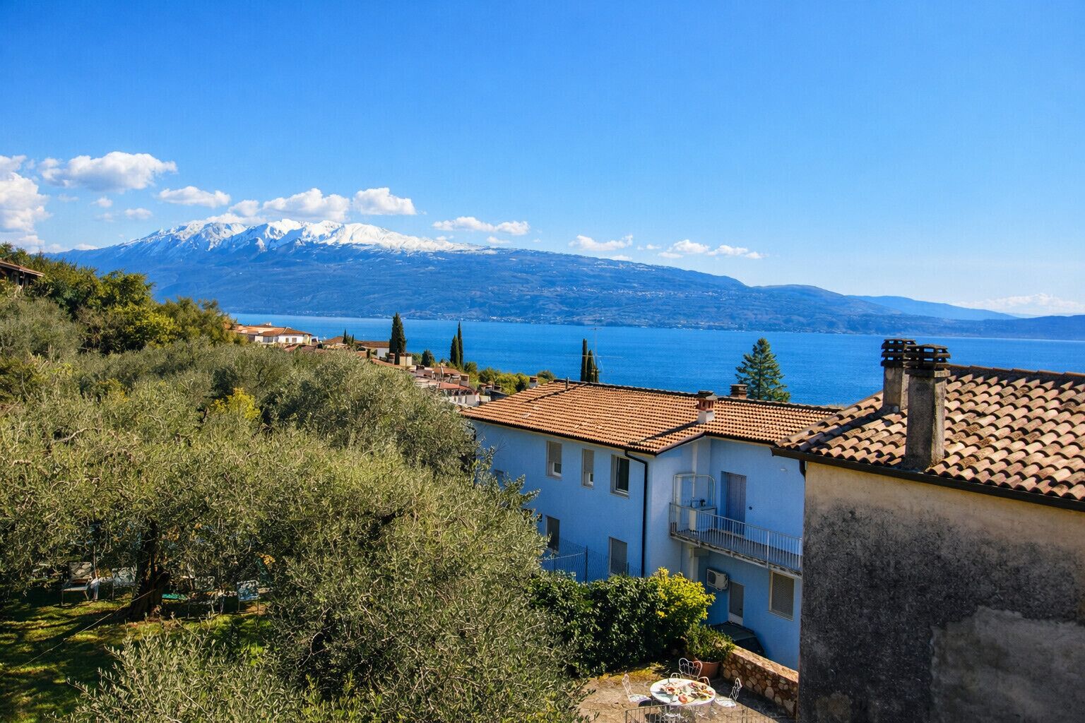 A coastal building with a tiled roof, a balcony, and a view of the sea and mountains.