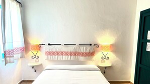 Una habitación de hotel con cama, dos lámparas de pared, una cortina y una puerta.