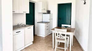Cocina compacta con armarios blancos, microondas integrado y un pequeño comedor con mesa y sillas.