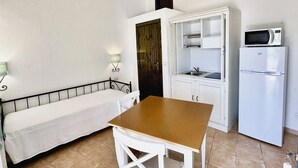 Una kitchenette compacta equipada con microondas, refrigerador y un pequeño comedor con banco y mesa.
