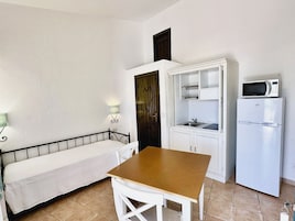 Una kitchenette compacta equipada con microondas, refrigerador y un pequeño comedor con banco y mesa.