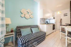 Ein modernes Wohnzimmer mit einem gemusterten Sofa, einem kleinen Tisch mit einer Lampe und einer Küchenzeile mit Kühlschrank und Herd.