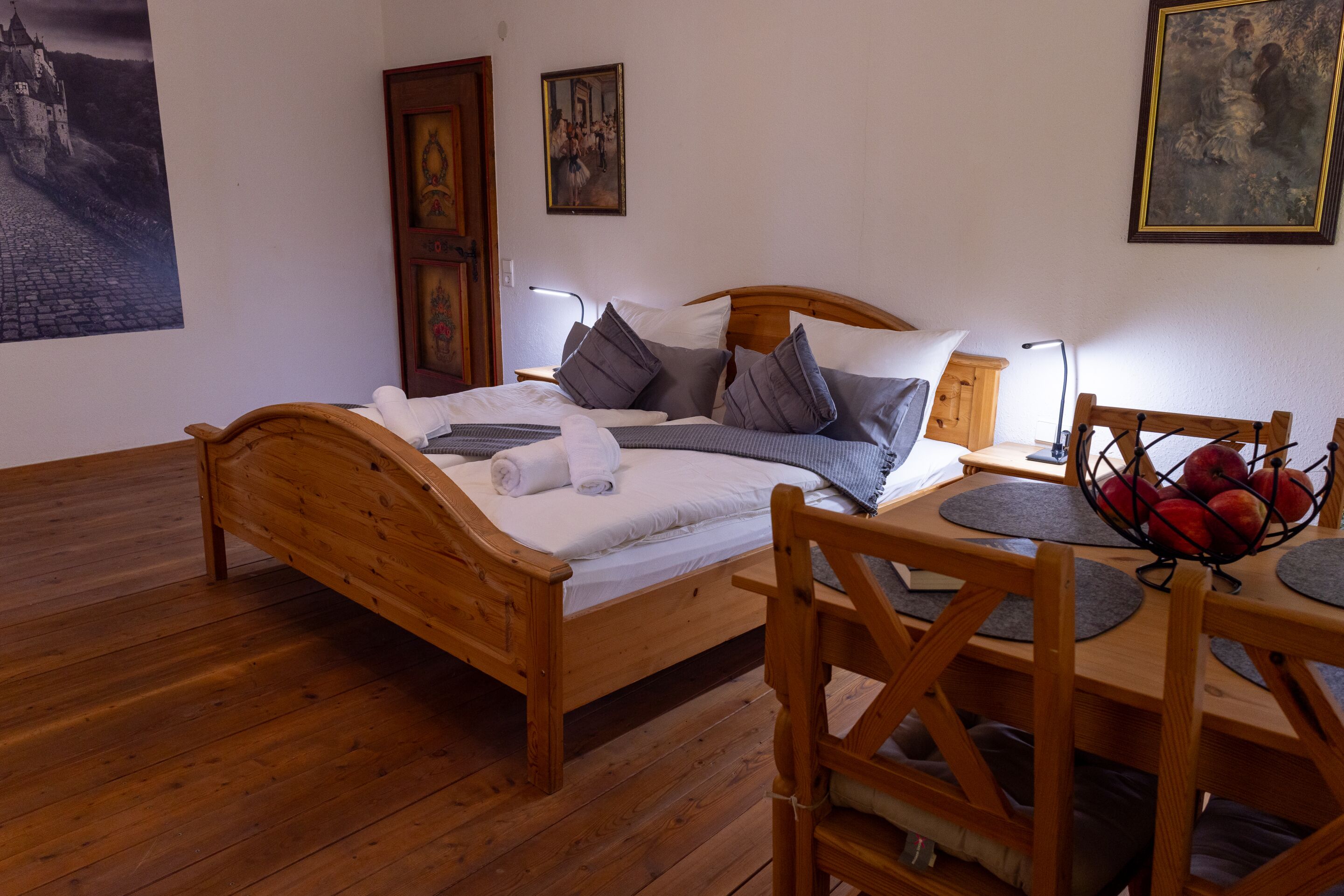 A wooden bed with pillows, a bedside table with a lamp, and a fruit basket.