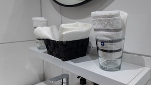 A bathroom with a white shelf holding a black basket and a glass with a towel.