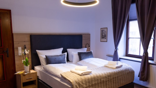 A neatly made bed with a headboard, a bedside table with a lamp, and a window with curtains.