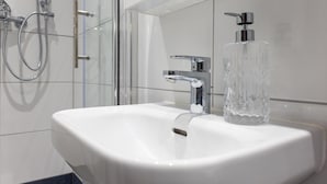 A bathroom with a white sink, chrome faucet, and a clear glass soap dispenser.