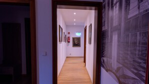 A hallway with wooden flooring, framed artwork on the walls, and a fire extinguisher.