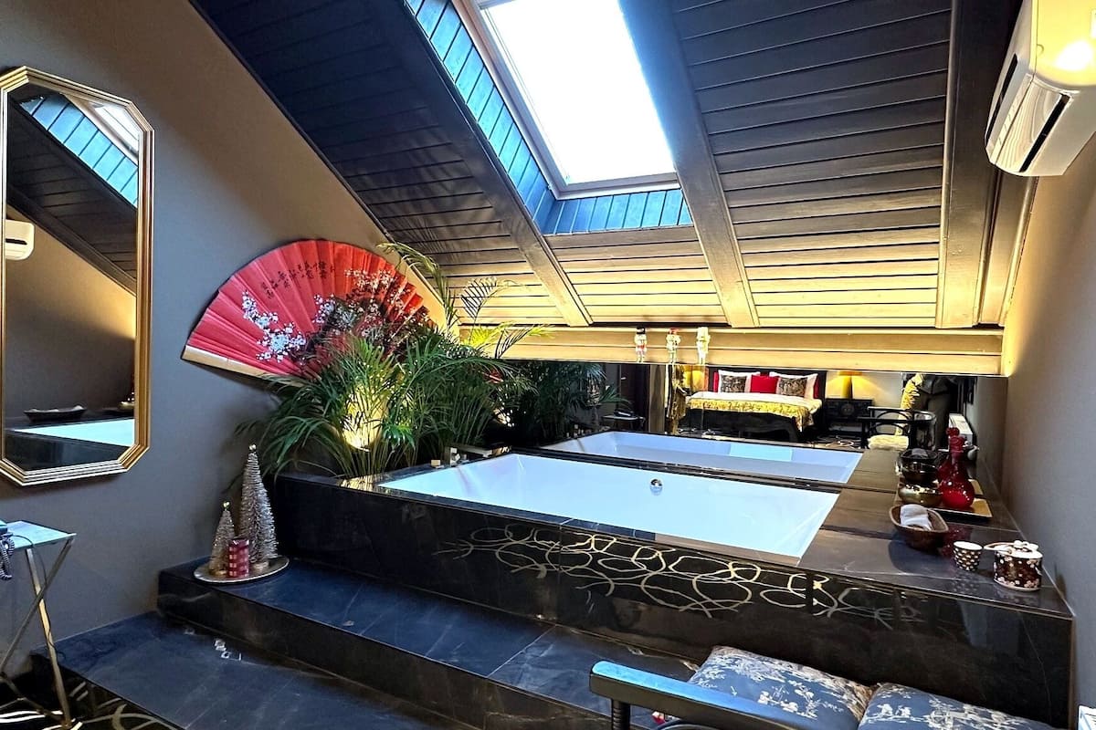 A modern bathroom with a large mirror, a red fan, and a bathtub.