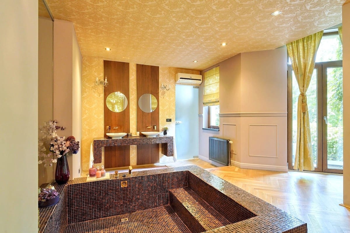 A bathroom with a large bathtub, two sinks, a mirror, and a radiator.