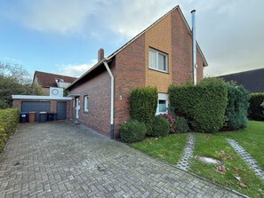 A two-story brick house with a paved driveway, a garage, and a well-maintained garden. - North Sea dream Horumersiel - 120 m² apartment | garden & fireplace | 800 m to the beach (Wangerland)