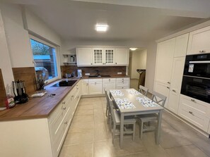 A modern kitchen with white cabinets, a wooden countertop, a dining table with chairs, and a built-in oven. - North Sea dream Horumersiel - 120 m² apartment | garden & fireplace | 800 m to the beach (Wangerland)